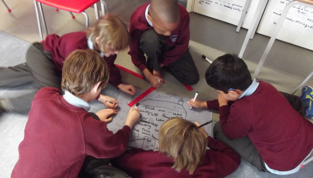 Primary school children in a circle on the floor drawing a house picture