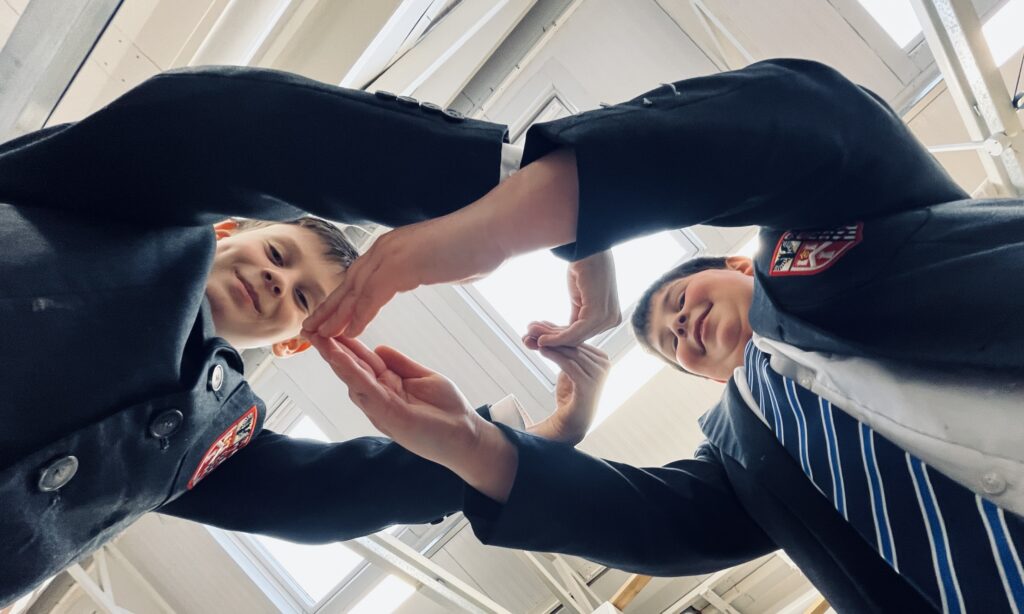 Two young boys in school uniform make a heart shape.